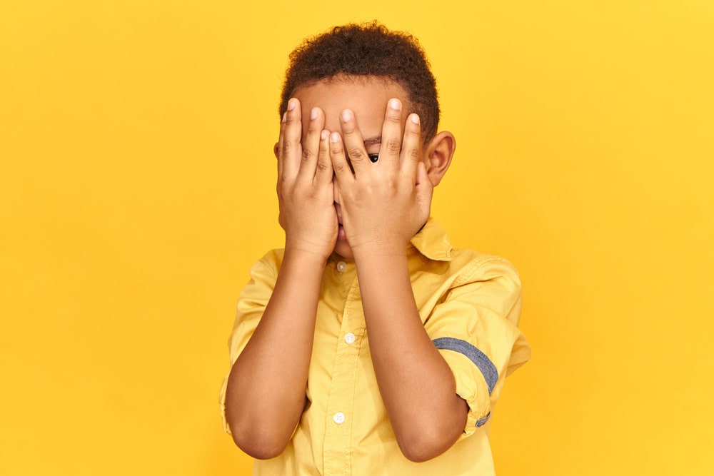 Un jeune enfant gêné se cache derrière ses mains pour montrer sa timidité
